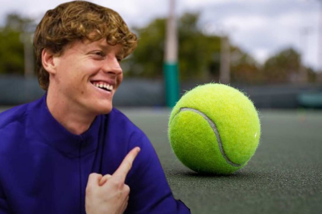 Jannis Sinner sorridente indica una pallina da tennis