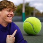 Jannis Sinner sorridente indica una pallina da tennis